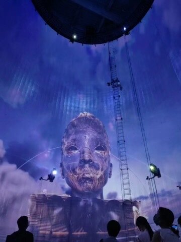 A large translucent face installation rising inside a silo