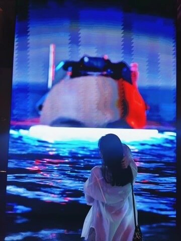 A visitor photographing a large LED screen over a reflective floor